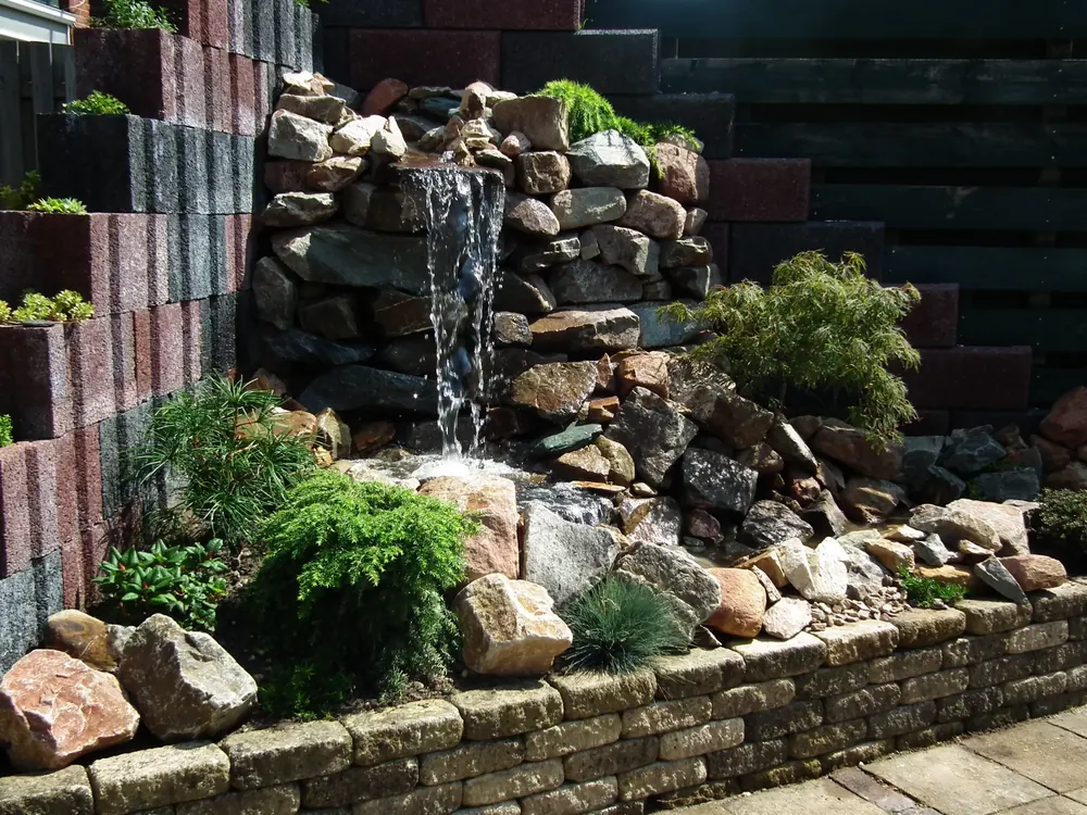 Waterval van natuursteen die uitmondt in een vijver met oeverbeplanting