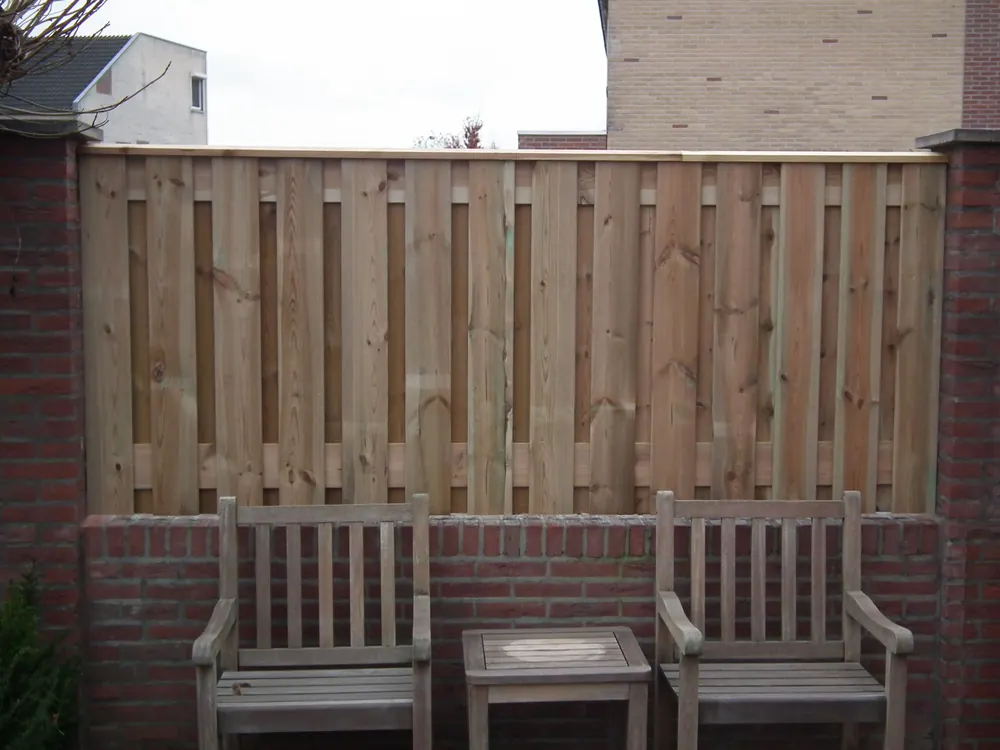 Houten schutting op betonnen poeren, afgewerkt met een dekplank